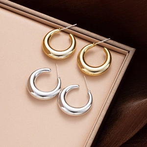 Macro shot of minimalist gold and silver C-shape stud earrings on a satin jewelry display