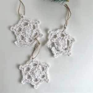 Close-up of three white crochet snowflake ornaments with rustic jute hanging ropes