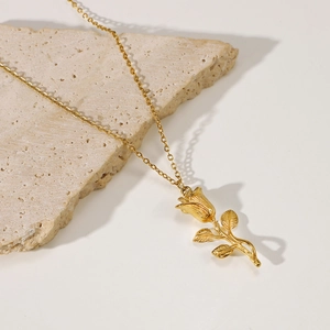 Elegant 18K gold plated rose flower pendant necklace displayed on a textured stone base