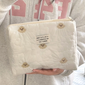 Detail of cream quilted makeup bag featuring brown character embroidery and textile tag