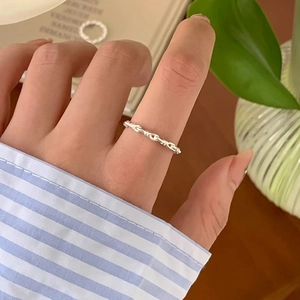 Detail of silver twisted chain ring worn on finger with minimalist wavy metal design