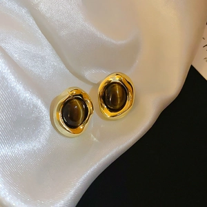 Detail of gold-plated tiger eye stud earrings on elegant white satin background