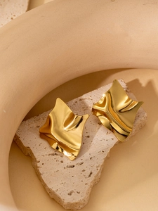 Close-up of irregular wave-shaped gold earrings on textured beige stone surface