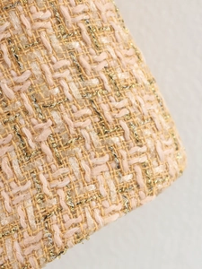 Close-up of premium tweed fabric in peach and beige tones with shiny golden lurex threads