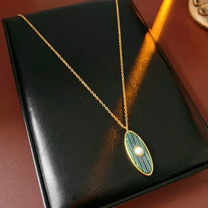Detail view of a vintage gold sunburst oval pendant with green enamel and center pearl