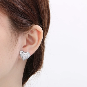 Dettaglio di orecchini a lobo a forma di cuore in argento indossati da una donna