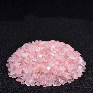 Polished natural rose quartz crystal chips stacked on a minimalist dark matte background