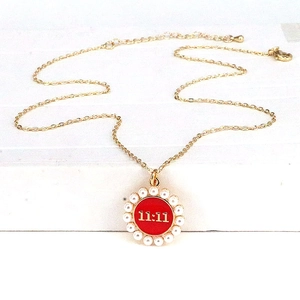 Detail of gold lucky 11:11 necklace with red enamel and white pearls on white background
