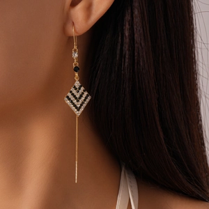 Detail of geometric rhombus tassel earrings with black and white crystals in gold plating