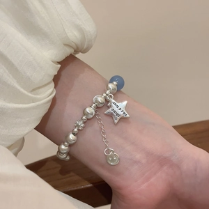 Detail of silver beaded bracelet with star and flower charms on a woman's wrist