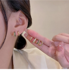 Close-up of small gold hoop earrings with black enamel and zircon inlay on model's ear