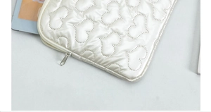 Detailed close-up of heart quilted texture and silver zipper on white tablet sleeve