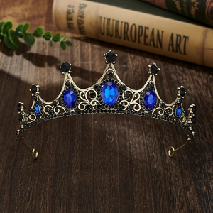 Macro shot of vintage gold tiara with blue oval gems and black crystals on wooden desk