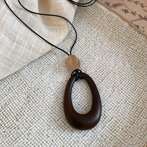 Detailed view of the dark brown oval resin pendant with amber bead on a black cord
