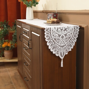 White lace table runner with intricate hollow patterns and decorative tassels on wood