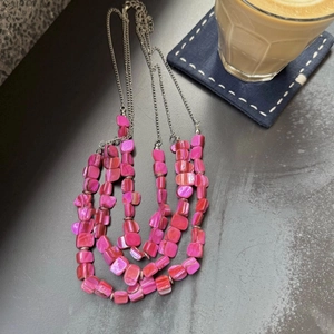 Detail of layered silver necklace featuring vibrant magenta shell-like iridescent beads