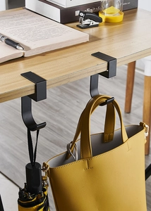 Macro shot of matte black metal desk hook holding a bag on a wooden table edge
