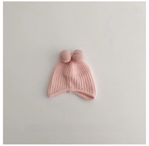 Detailed view of pink knitted baby hat with soft vertical ribs and double pom-poms