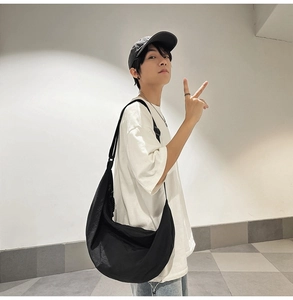 Grand sac besace noir en nylon pour homme porté avec un t-shirt blanc décontracté