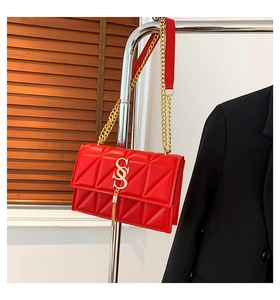Macro detail of red textured crossbody bag with gold logo and stylish metal tassel