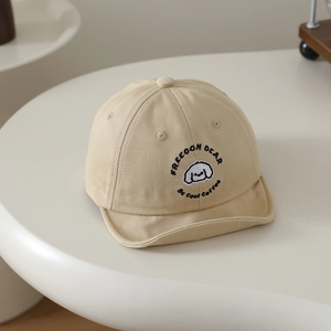 Détail de la broderie chiot et des lettres sur la casquette beige à visière souple bébé
