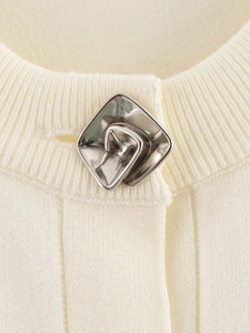 Detalle macro del cuello de cárdigan de punto blanco crema con botón de flor metálico
