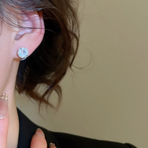 Close-up of a silver stud earring featuring a large round-cut sparkling crystal on ear