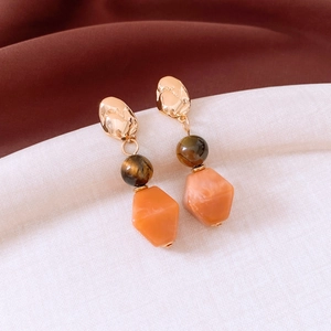Detailed shot of irregular gold stud earrings with tiger eye bead and orange resin pendant