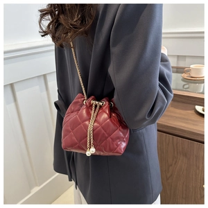 Detail view of quilted burgundy bucket bag with gold chain and pearl drawstrings