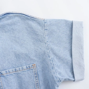 Detail of light blue denim romper featuring rolled cuffs and yellow contrast stitching