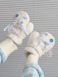 Close-up of white plush mittens featuring blue ribbon bows and delicate lace trim details