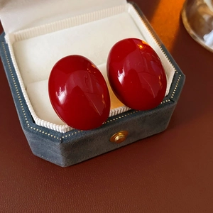 Close-up of elegant red enamel oval stud earrings on a velvet jewelry display box