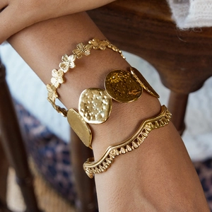Dettaglio di bracciali martellati dorati con accenti floreali e texture metallica ricca