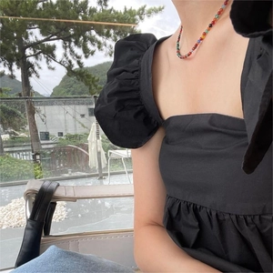 Close-up of a colorful beaded necklace worn with a black puff sleeve dress outdoors