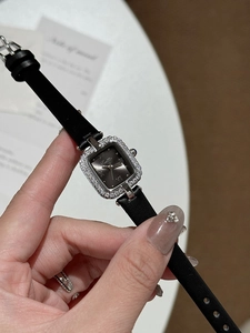 Gros plan d'une montre carrée en argent avec lunette sertie de diamants et bracelet noir