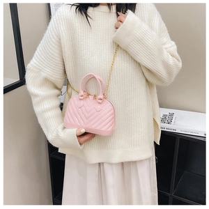 Close-up of pink jelly shell-shaped crossbody bag with gold chain strap on model