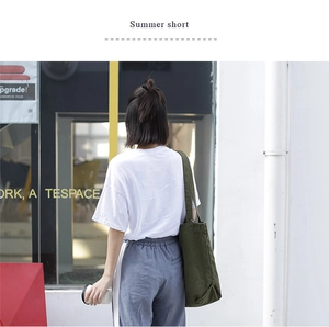 Outdoor shot of a woman wearing a dark green canvas tote bag with a white summer t-shirt