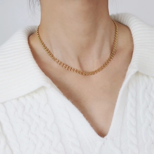 Detailed view of gold wheat-link choker necklace on a white knit sweater background