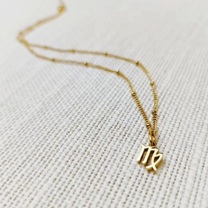 Macro detail of gold Virgo zodiac pendant on a delicate beaded satellite chain necklace