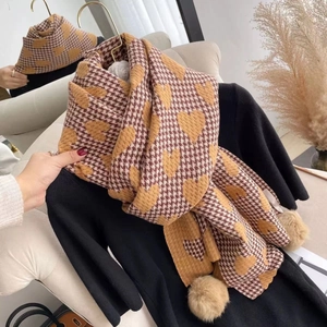 Close-up of houndstooth heart pattern scarf with pompom details on a black hanger