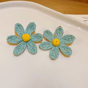 Gros plan de boucles d'oreilles fleurs bleues à texture tissée et cœur jaune dans un plat