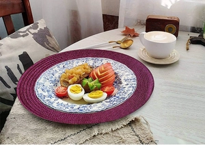 Close-up of purple round braided placemat on wooden table with elegant breakfast setting