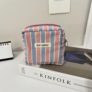 Detailansicht der gestreiften Canvas-Kosmetiktasche mit Ring-Reißverschluss auf Buch