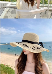 Detail of beige straw sun hat featuring black Hello Sun embroidery and a ribbon bow