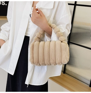 Detail of a beige plush cylindrical handbag with decorative fuzzy ball top handles