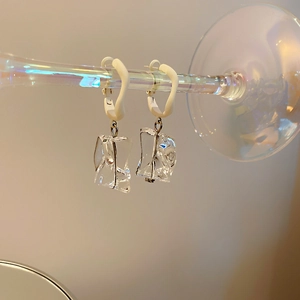 Detailed shot of irregular clear acrylic earrings with white frosted hooks on glass