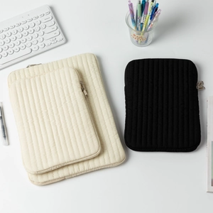 Quilted laptop and tablet sleeves in cream and black displayed on an office desk
