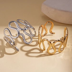 Minimalist wavy hollow cuff bracelets in gold and silver finishes on a textured background