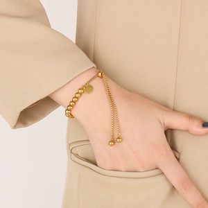 Gros plan d'un bracelet à billes dorées avec chaîne réglable porté avec un blazer beige