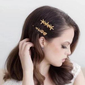 Close-up of a model wearing golden starfish and seashell hair clips in long brown hair